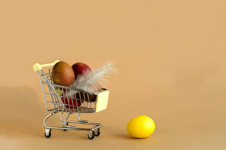 Easter eggs in a grocery cart on a beige background. A yellow egg lies separately. Easter background concept with copy spaceの写真素材