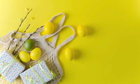 Easter yellow painted eggs, wrapped gifts, pussy willow sprigs lie on an eco bag on a yellow...