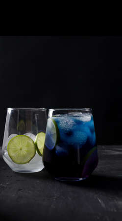 Blue cold drink in a transparent glass on a black background in a dark key, the second glass is out of focus with ice and a piece of lime, vertical backgroundの写真素材
