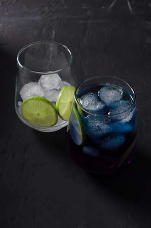 Blue tea with pieces of ice and lime in glass glass on a dark background, vertical background, selective focusの写真素材