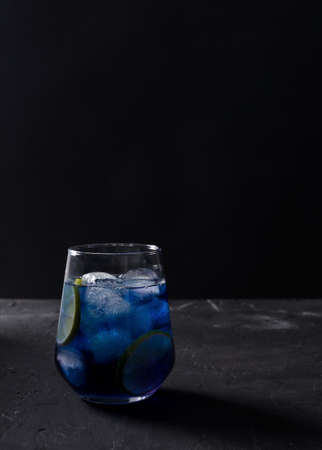 Blue cold drink in a transparent glass on a black background in a dark key, vertical background, copying textの写真素材