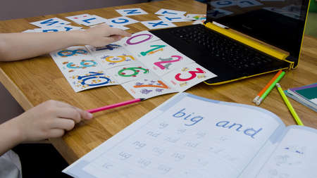 The concept of distance learning english. On the table are placed cards with numbers and a computer, the child's hands are on the tableの写真素材