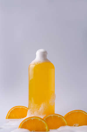 Shampoo, shower gel, orange liquid soap with natural ingredients in a transparent bottle on a light background in foam with orange piecesの写真素材