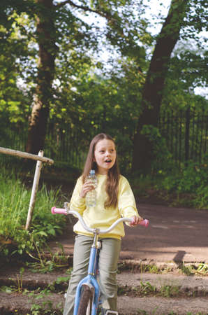 Surprise on the face of the child. A school-age girl on a bike in a park is surprised looking into the distance. Selective focusの写真素材