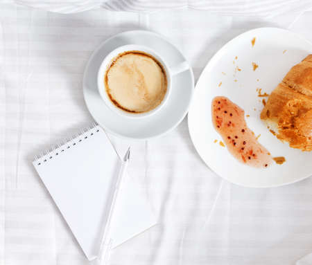 Morning breakfast in bed. A cup of coffee with a piece of croissal on a white backgroundの写真素材