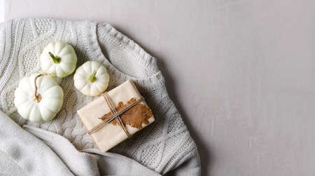Pumpkins and gifts in kraft paper on a knitted sweater on a beige background, warm cozy autumn concept, copying space, flat layoutの写真素材