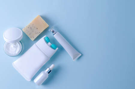 Cosmetic product for skin care of face, neck, decollete, eyes. Lifting cream with massage nozzle, natural soap, cream in tube and jar, hyaluronic serum in a bottle on a blue background, flat layout, copying textの写真素材