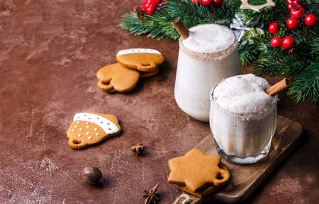 Egg punch, egg liqueur with Christmas tree branches, gingerbread and decor on a brown background. Eggnog Christmas drink in different glasses, selective focusの写真素材