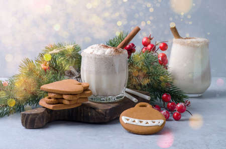 Two glasses with egg punch, egg liqueur in Christmas decor on a gray blue background. Christmas drink egg-nog with handmade gingerbread and bokehの写真素材