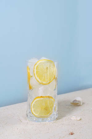 Summer cold drink in a glass on the sand with ice and lemon, vertical backgroundの写真素材