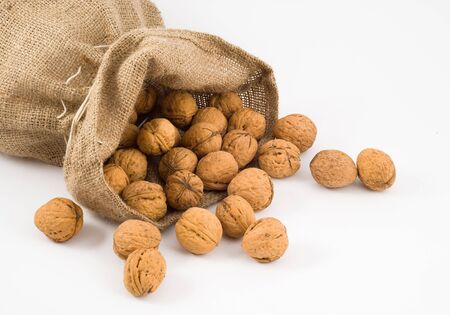 Burlap sack with walnuts spilling out over a white background の写真素材
