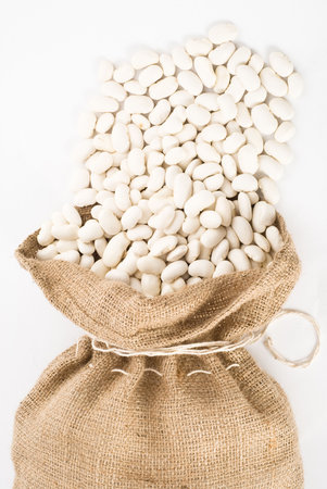 Burlap sack with white beans spilling out over a white background 