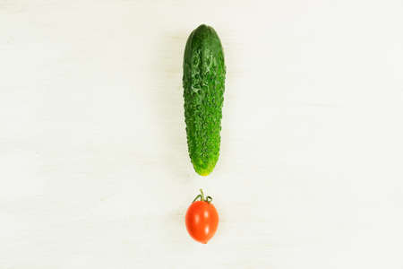 Ripe green cucumber and cherry tomato laid out on a white background in the form of an exclamation markの写真素材