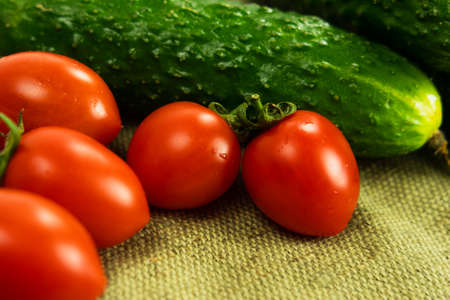 Ripe cherry tomatoes and cucumbers stacked on a tableclothの写真素材