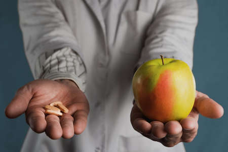The doctor holds a pill and an apple in his hands. The concept of choosing between artificial drugs or vitamins and natural productsの写真素材