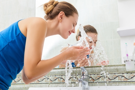 Young woman washing her face with clean water in bathroomの写真素材