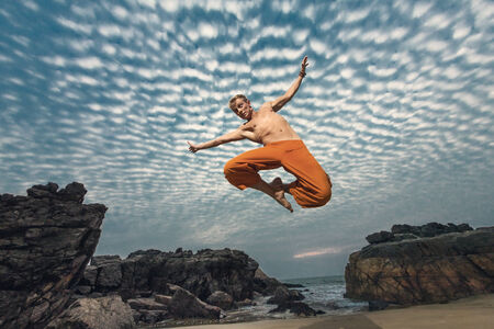 Young man high jumping on beach with sunset sea view at backgroundの写真素材