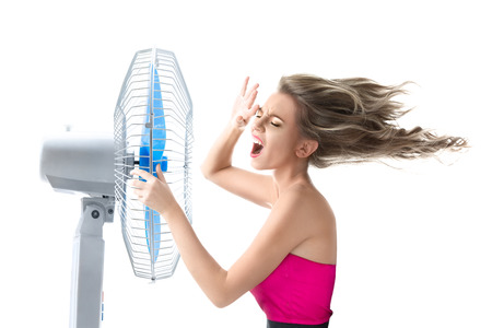 Young woman cooling face under wind of cooler fan isolated on white backgroundの写真素材