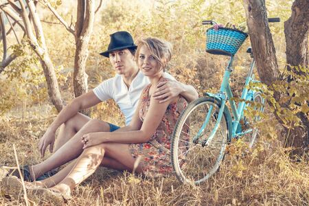Young woman and man with retro bicycle sitting on a grass in a park - outdoor portraitの写真素材