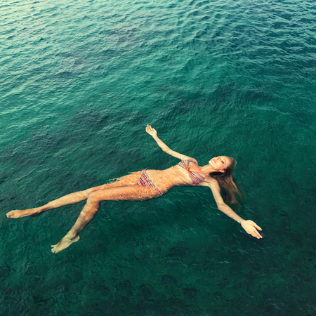 Young slim woman lie on back and relaxing in blue sea waterの写真素材
