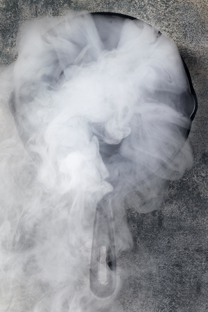 Frying pan with cloud of smoke on black stone surfaceの写真素材