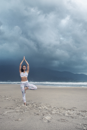 Young sporty slim woman doing yoga exercise on sand of the tropical sea beach with space for textの写真素材
