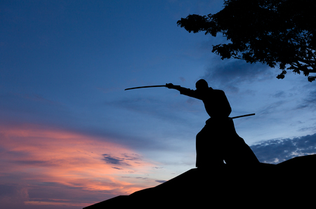 Abstract photo of man silhouette demonstrating martial arts with sword in front of sunset skyの写真素材
