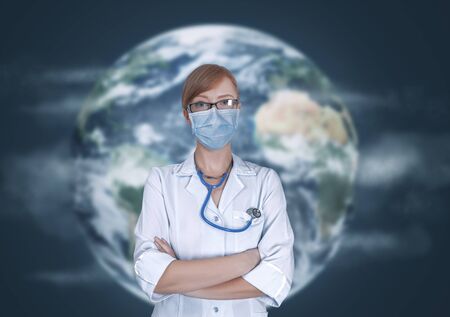 Concept of medical doctors fighting against global pandemic virus. Portrait of young woman in medical uniform and mask protect world from corona virus outbreak in front of Earth globe.の写真素材