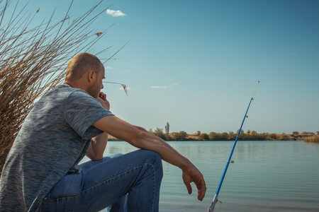 Fisherman with rod fishing alone on the river bank. Enjoying calm and relax of natureの写真素材