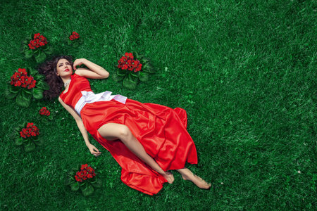 A serene impression of a young woman in a red dress lying on her back on the grass, offering ample space for personalized text or objectsの写真素材