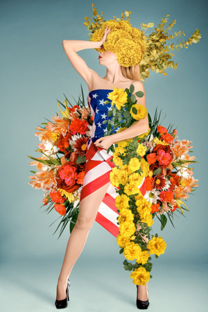 A full-length portrait of a young woman wearing a dress adorned in patriotic USA flag colors. This studio shot on a neutral background captures the beauty of a woman embracing both patriotism and floral elegance, making it perfect for Fourth of July celebrations and fashion-themed designs.の写真素材