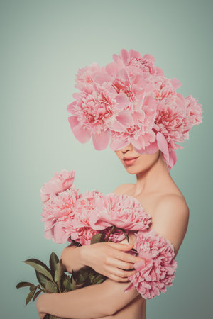 A serene and elegant woman embraces vibrant pink peony blooms, her face partially obscured behind the lush petals. Symbolizing femininity, natural beauty, and renewal. For cosmetics, fashion, or floral branding.の写真素材