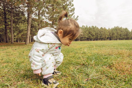 Joyful Toddler Girl in Floral Jumpsuit Running Through Autumn Pine Forest Park, Outdoor Childhood Adventure and Nature Explorationの写真素材