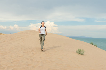 Woman hiking on sandy dunes near ocean. Perfect for travel, adventure, or fitness concepts. Ideal for promoting outdoor activities, healthy lifestyles, or coastal destinations.の写真素材