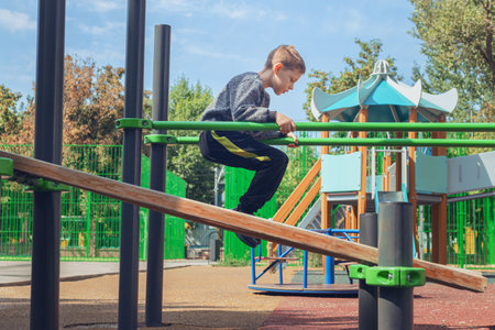 Smiling boy hanging from exercise rings in outdoor playground. Autumn trees in background. Perfect for promoting children's fitness, outdoor play, and active lifestyles.の写真素材