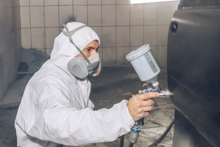 Skilled worker using spray gun to paint car body in workshop. for automotive repair, vehicle customization, or industrial craftsmanship concepts.の写真素材
