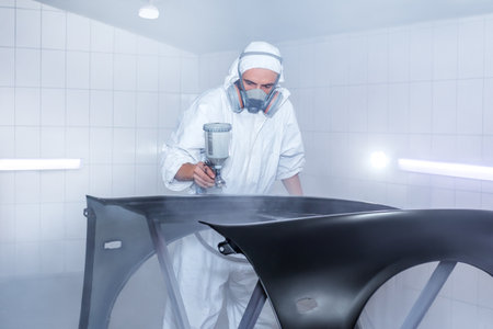 Skilled worker using spray gun to paint car body in workshop. for automotive repair, vehicle customization, or industrial craftsmanship concepts.の写真素材