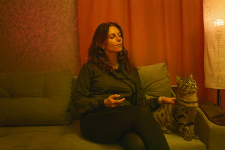 a brunette woman embracing her cat on a red couch, bathed in pink and purple neon light. for themes of pet companionship, relaxation at home, or modern lifestyle imagery.の写真素材