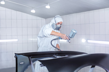 Skilled worker using spray gun to paint car body in workshop. for automotive repair, vehicle customization, or industrial craftsmanship concepts.の写真素材