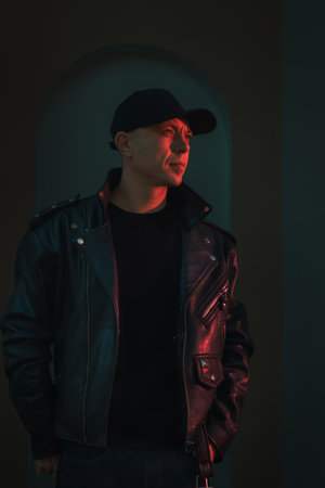 Moody fashion portrait featuring model in leather jacket with dramatic red and green neon lighting. Urban fashion campaigns, music industry visuals, and edgy lifestyle content.の写真素材