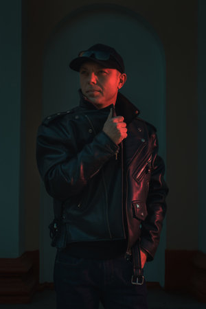 Moody fashion portrait featuring model in leather jacket with dramatic red and green neon lighting. Urban fashion campaigns, music industry visuals, and edgy lifestyle content.の写真素材