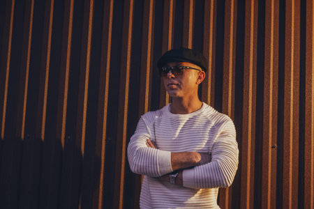 Modern urban portrait of fashionable young man in casual streetwear against geometric striped background. Fashion blogs, lifestyle magazines, and urban style campaigns.の写真素材