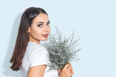 A person holding a fresh bouquet of lavender flowers against a light blue background. for wellness, beauty, lifestyle, natural cosmetics, or spa marketing materials.の写真素材