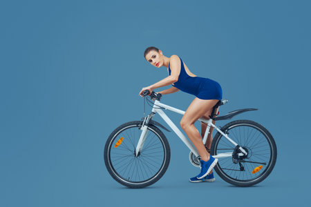 A female athlete on a bicycle in a studio. for themes of sport, fitness, health, training, energy, and an active lifestyle.の写真素材
