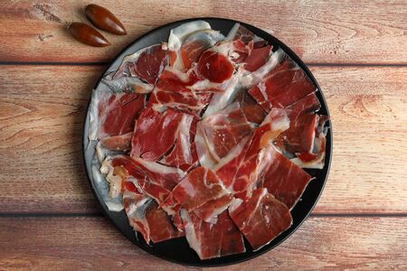 Ration of acorn-fed Iberian ham on a black plate on a rustic wooden tableの写真素材
