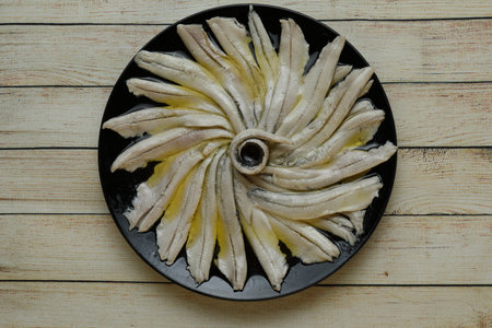 Portion of anchovies in vinegar on black plate on wooden table top view