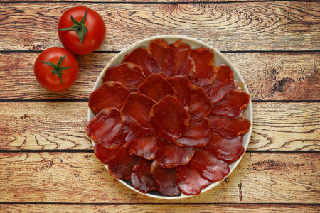 Serving of acorn-fed Iberian loin on black plate with wooden background garnished with two tomatoesの写真素材