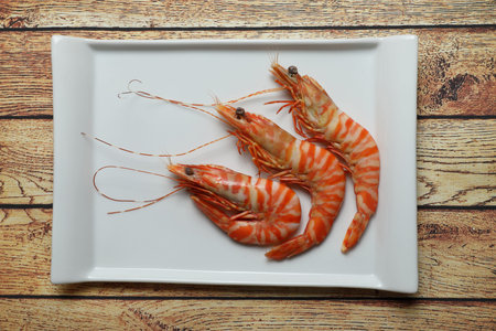 Three tiger prawns in white rectangular plate on rustic wooden table