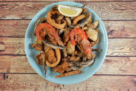 Portion of fried fish (anchovies, bienmesabe, squid, cod and prawns) in black plate on rustic wooden...