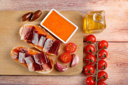 Portion of acorn-fed Iberian ham on a white plate, on a rustic wooden table and decorated with...